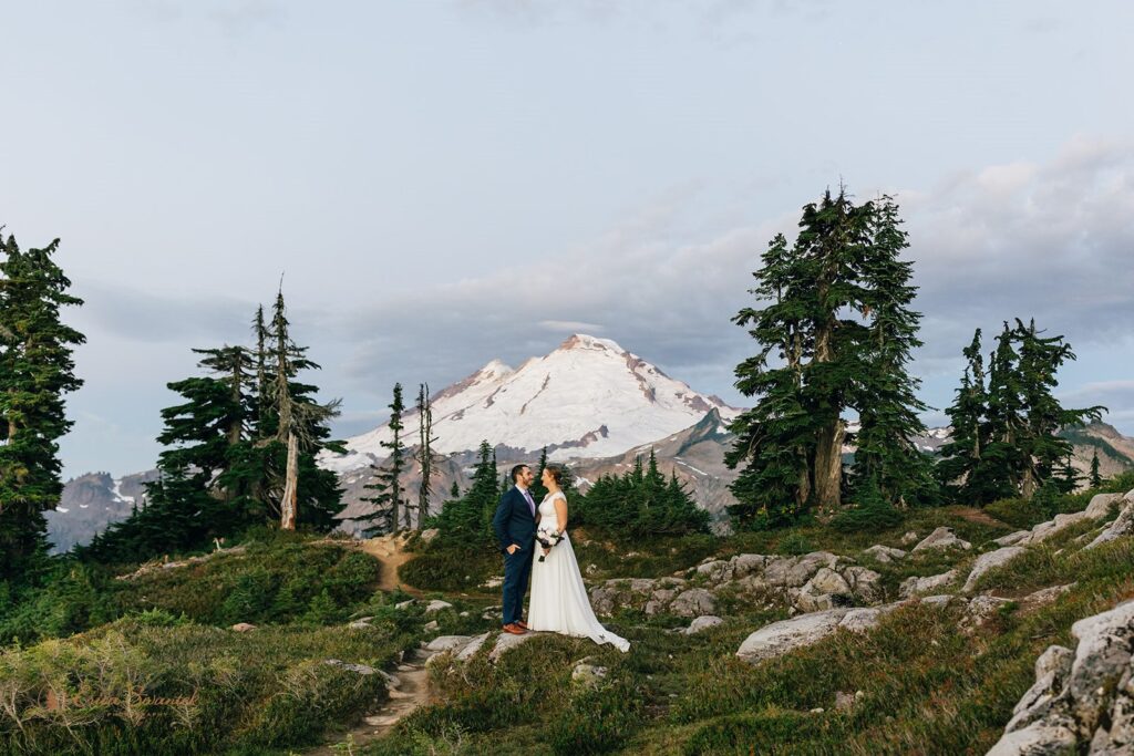 A couple stands in front of a snowy Mt. Baker during their Sunrise elopement at Artist Point. 
