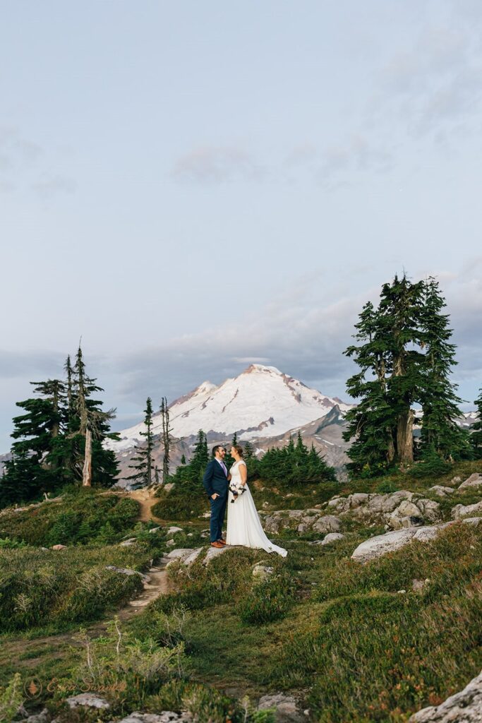 A groom dressed in a navy suit stands with his bride in front of a snowy mountain during their Artist Point elopement. 
