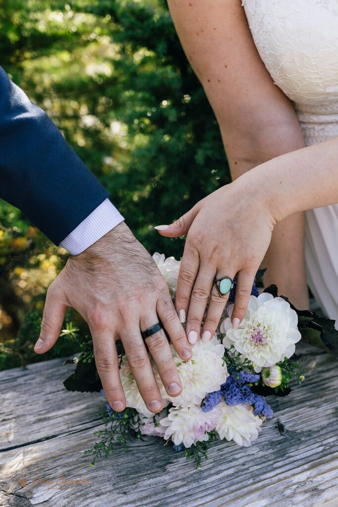 A groom and bride showcase their wedding rings alongside a bright bridal bouquet. 