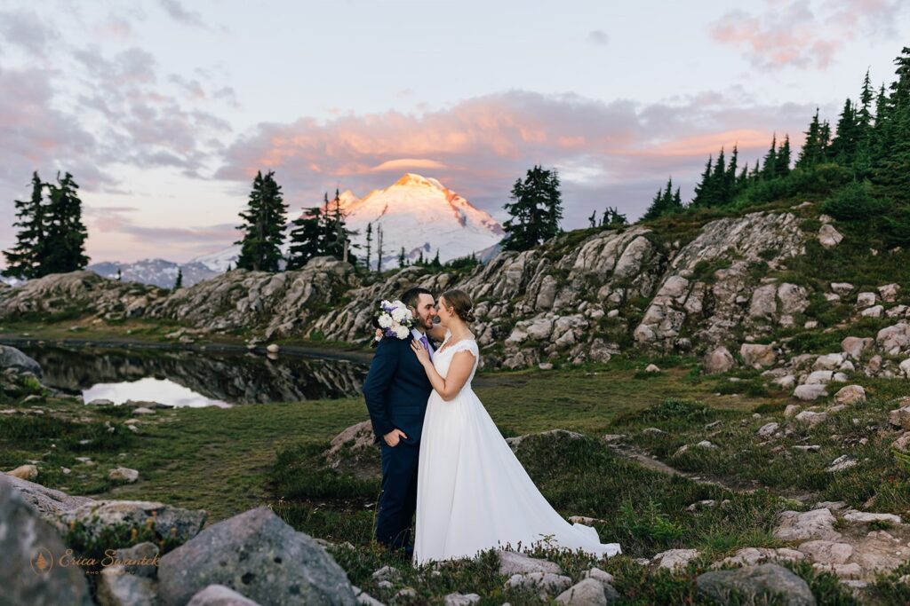 A couple poses for a Sunrise wedding portrait in front of a snowy Mt. Baker during their Sunrise elopement at Artist Point. 