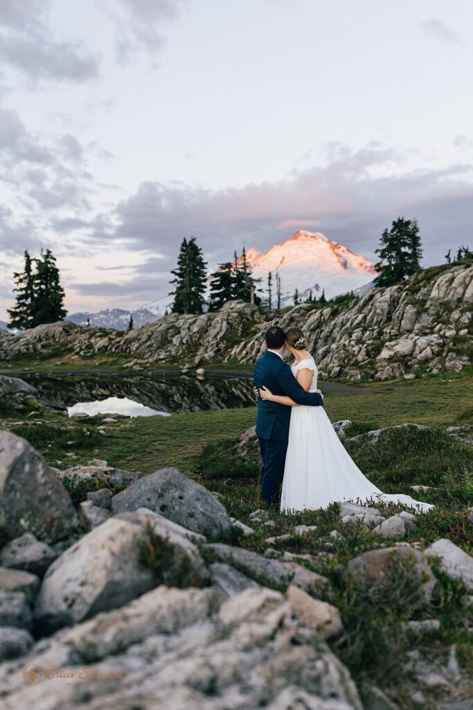 A Washington elopement couple embraces while admiring a snowy Mt. Baker during their Sunrise vow ceremony. 