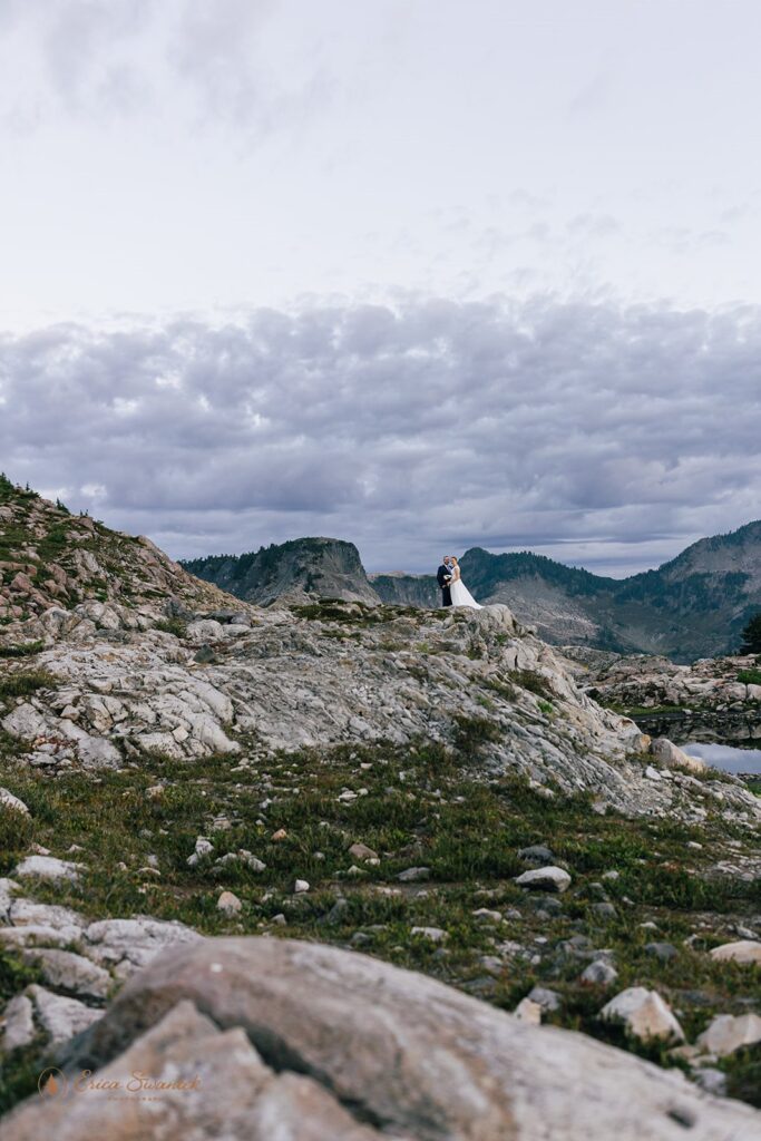 A North Cascades elopement couple stands long a cliff in the distance. 
