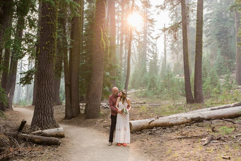 A bride and groom in casual elopement attire embrace in a forest in Crater Lake National Park at Sunset. 