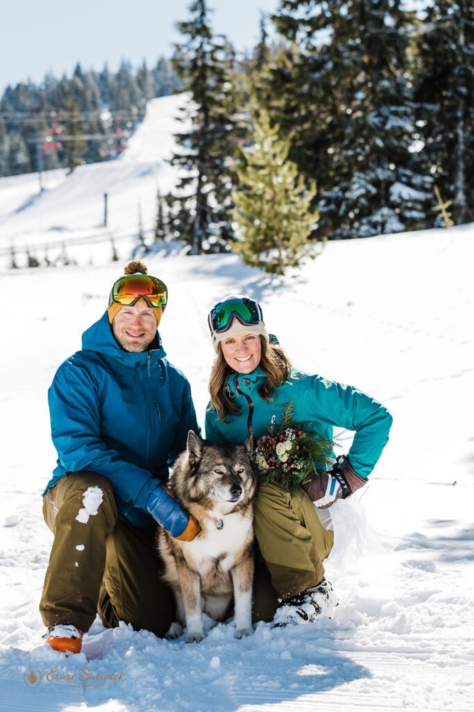 A bride and groom dressed in ski attire pose with their dog on the slopes of Mt. Bachelor during their winter elopement. 