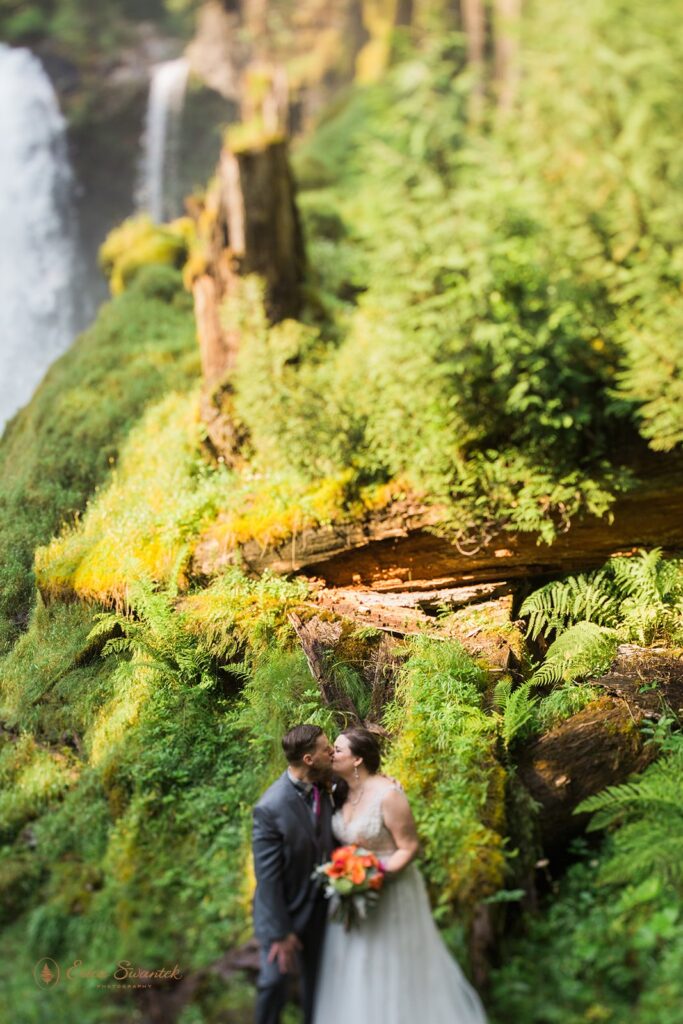 A Sahalie Falls elopement couple embrace and kiss near the base of the Oregon waterfall. 