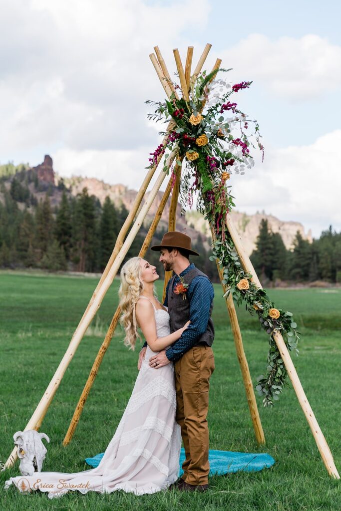 An Oregon elopement couple embraces beneath a bohemian wedding arch at Wine Down Ranch. 