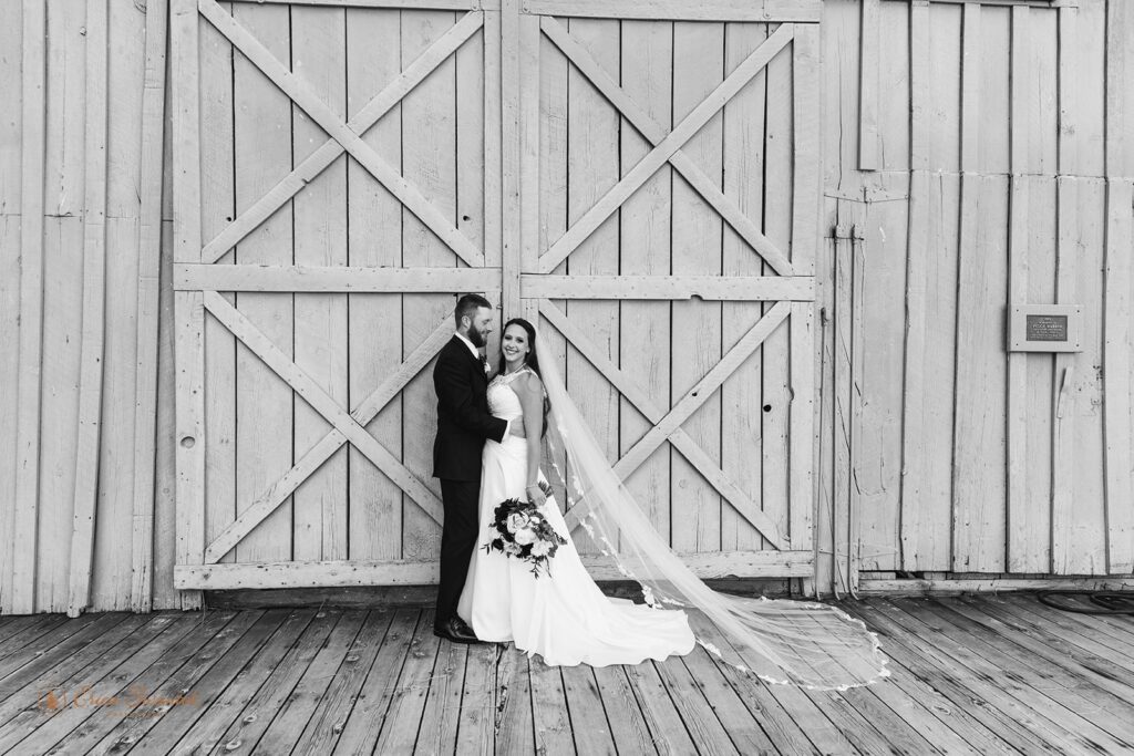 A couple dressed in formal wedding attire pose in front of a barn door at Black Butte Ranch in Sisters, Oregon. 