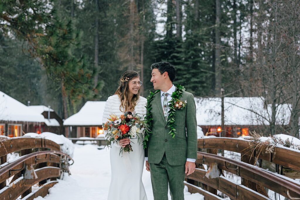 A Lake Creek Lodge wedding couple admires one another while walking across a snowy bridge in Winter.