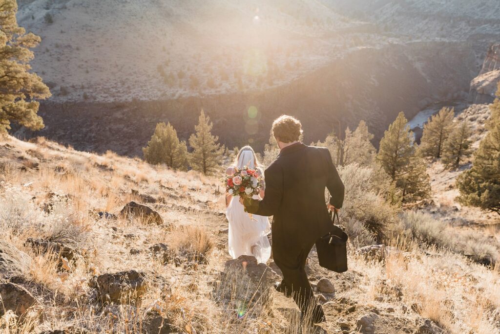 A groom wearing a black suit follows his bride down a hillside during their Bend, Oregon, elopement.