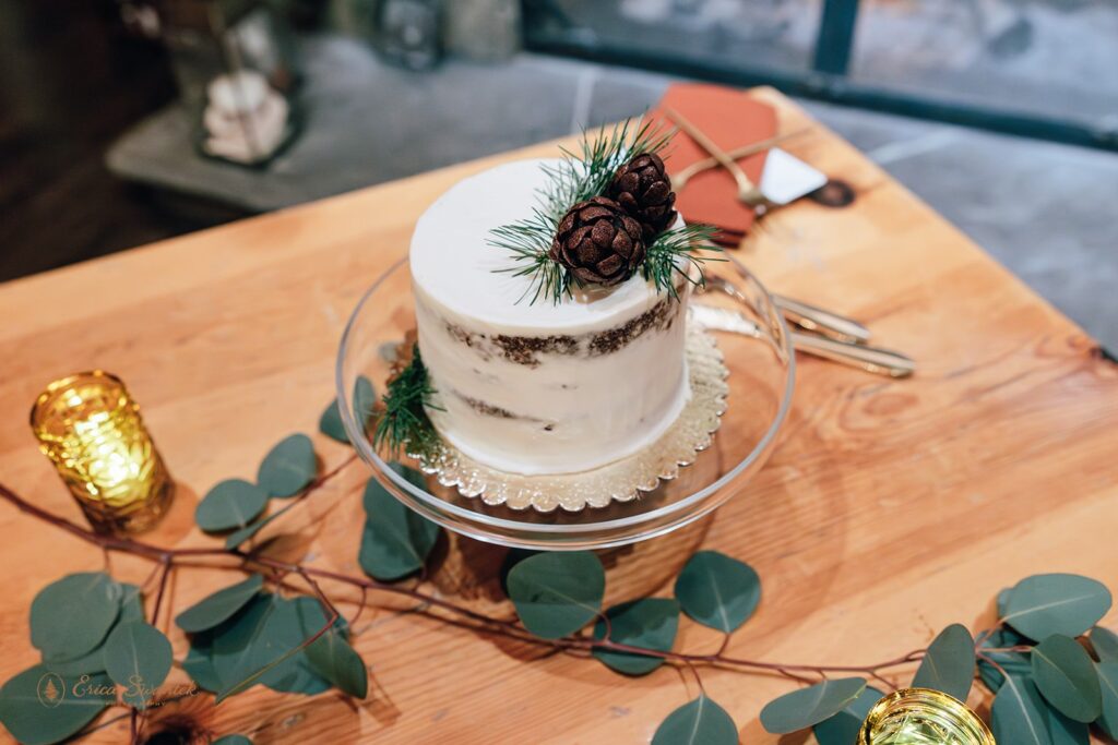 A naked wedding cake accented with pine needles and pine cones. 