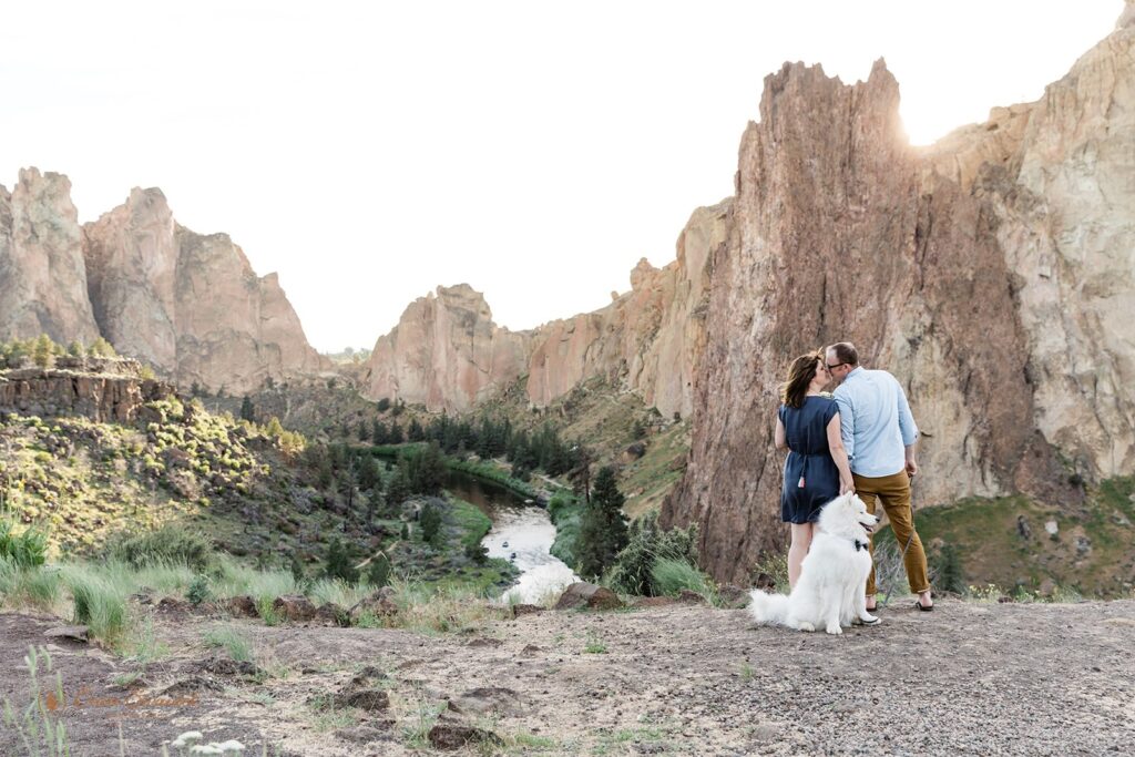 A Smith Rock State Park elopement couple kiss at Sunset with their white, fluffy dog nearby. 