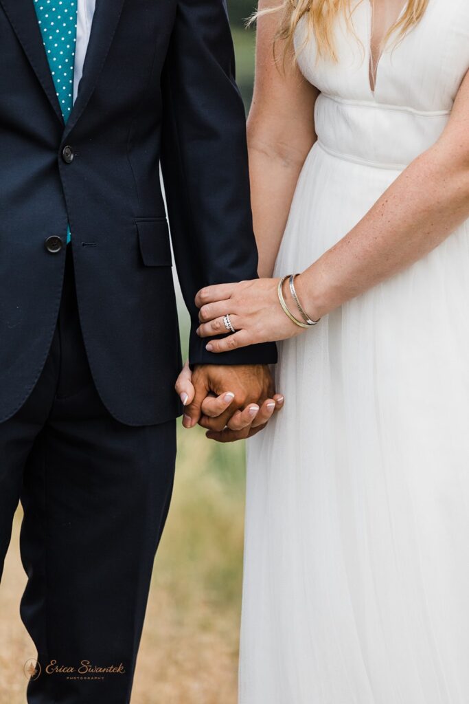 A groom wearing a navy wedding suit and teal, polka dot tie holds his bride's hand, who is wearing a traditional white wedding dress. 