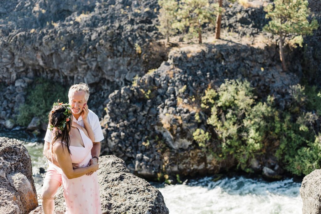 A bride and groom embraces above Tumalo Falls during their outdoor Oregon elopement. 