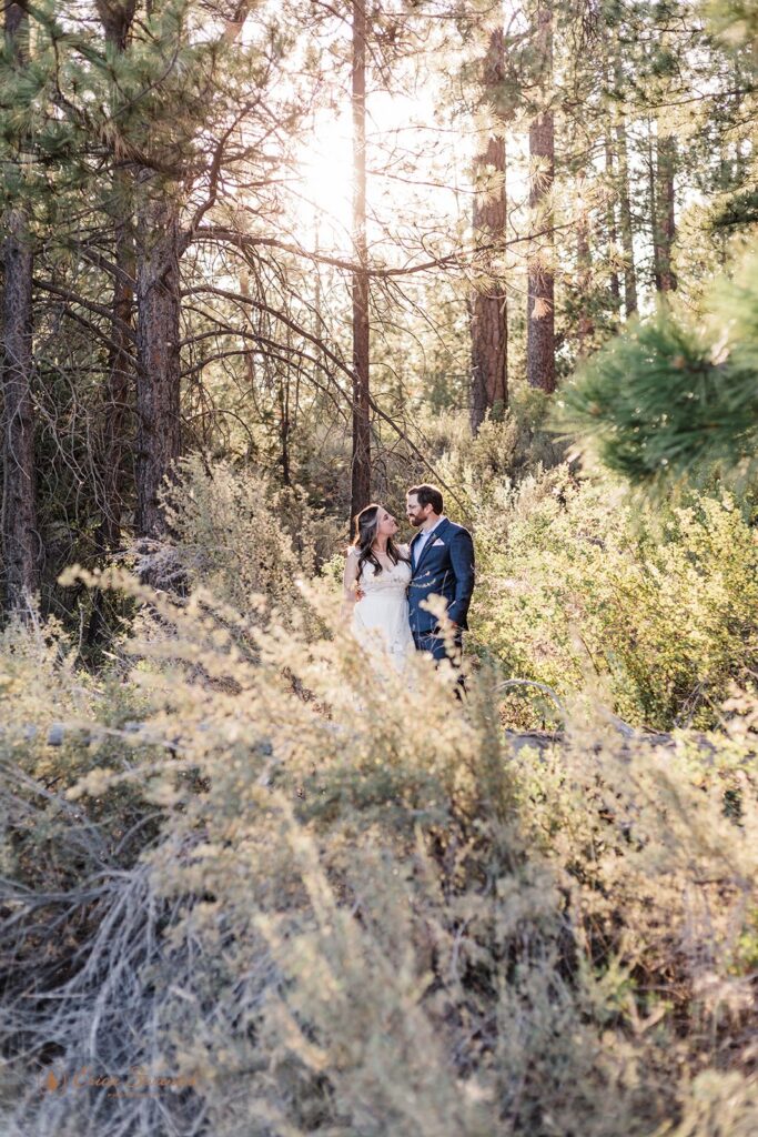 A bride in a white wedding dress hugs her groom, who is wearing a navy wedding suit, during their hiking elopement along Deschutes River Trail.
