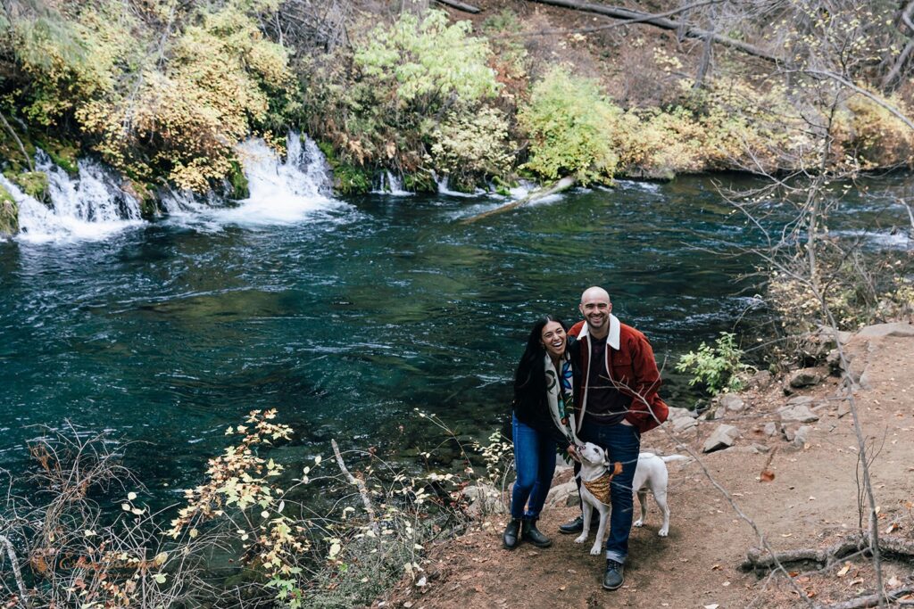 An Oregon elopement couple pose for a portrait with their dog alongside Metolius River near Bend, Oregon.