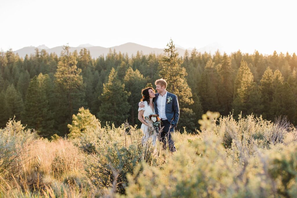 An Oregon intimate wedding couple embrace in a meadow near an evergreen forest at Shevlin Park. 