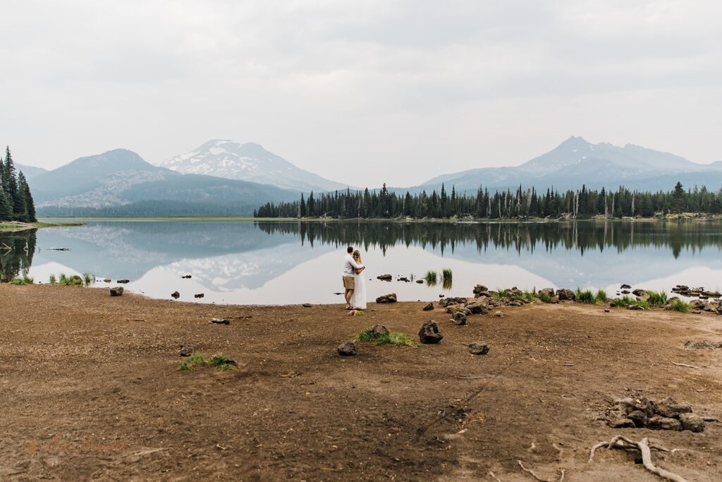 An elopement couple embraces on the shores of Sparks Lake, an intimate Bend wedding location.