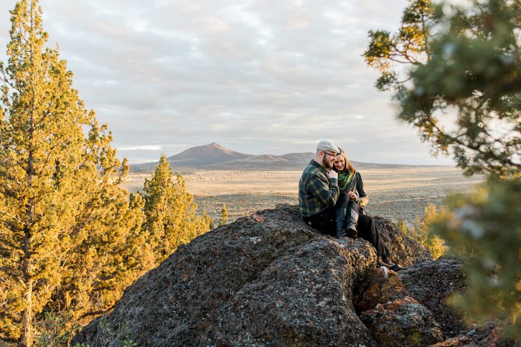 A hiking elopement couple sits atop a rock overlooking Crooked River Grasslands near Bend, Oregon. 