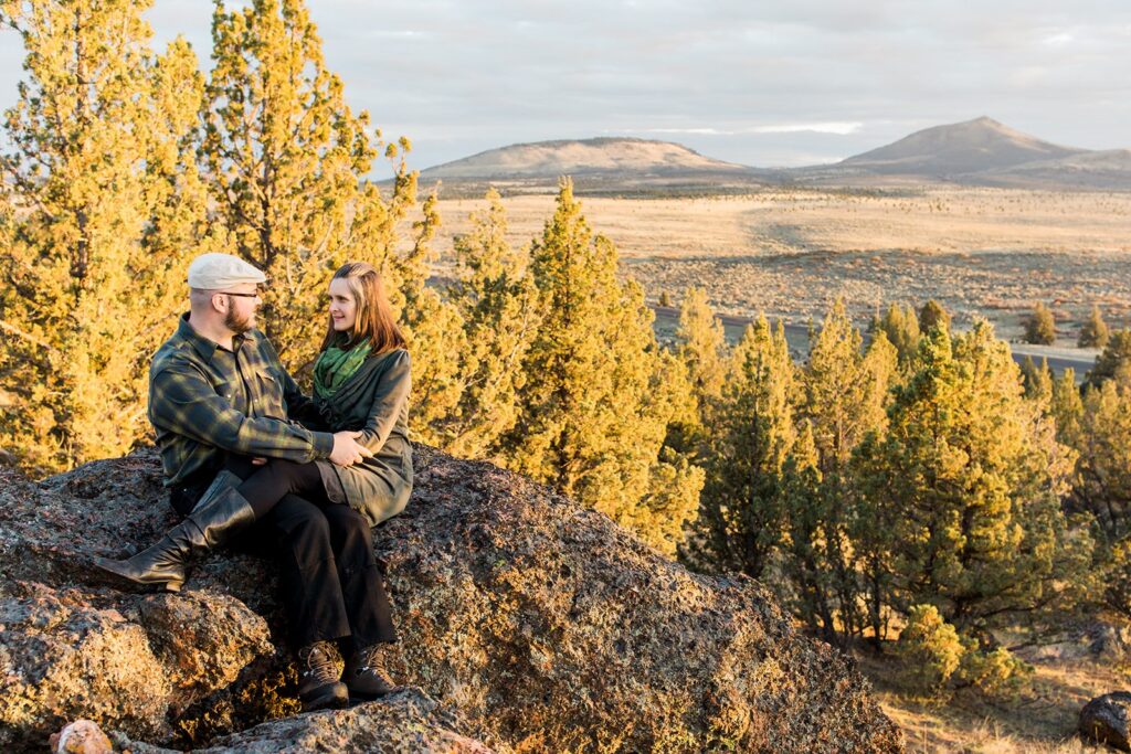 An Oregon couple sits atop a rock overlooking Crooked River Grasslands at Sunset. 