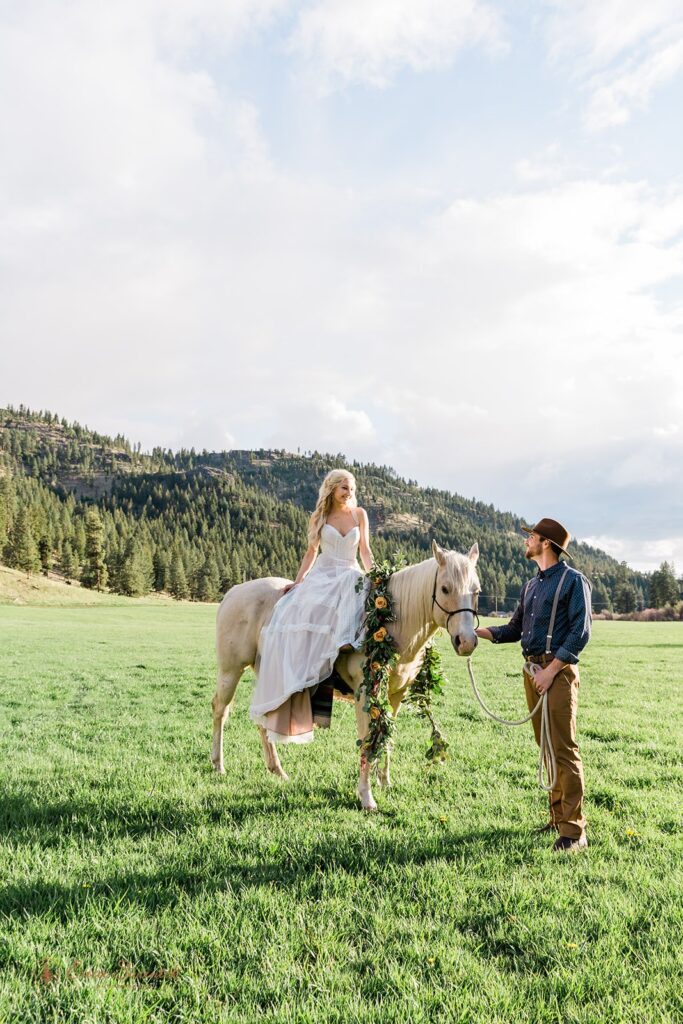 A boho bride sits atop a horse being led by her groom at Wine Down Ranch. 