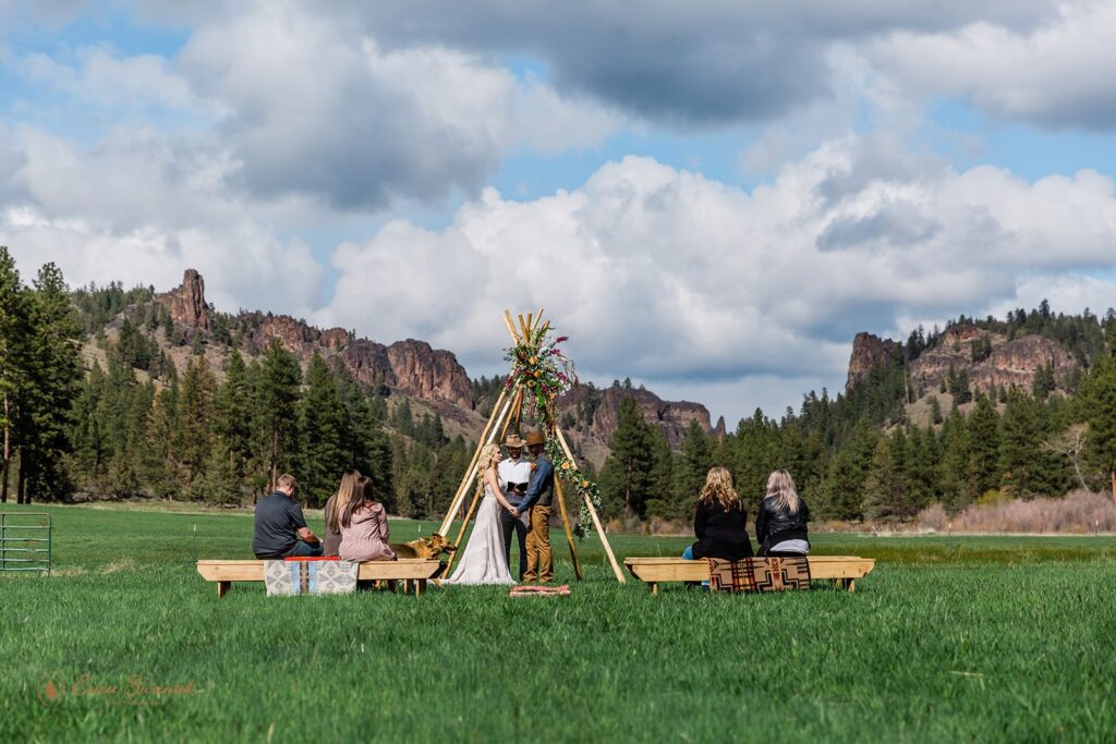 A boho elopement couple recites vows beneath a teepee arch decorated with burgundy and apricot roses at Wine Down Ranch. 