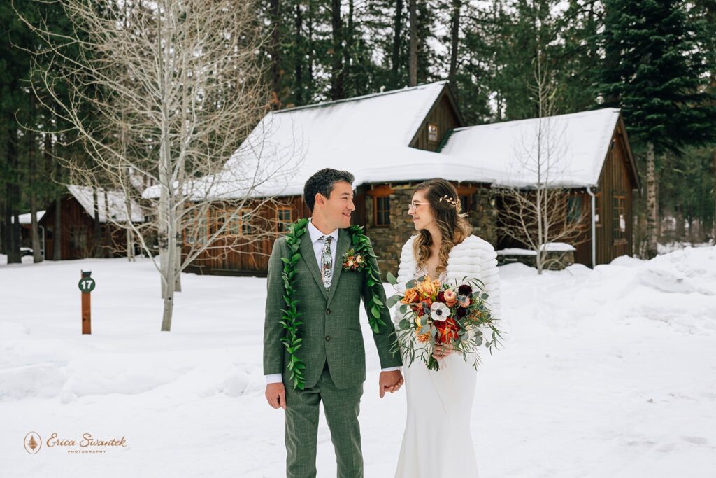 A groom dressed in a forest green suit and Maile Lei holds his bride's hand at Lake Creek Lodge in Winter. 