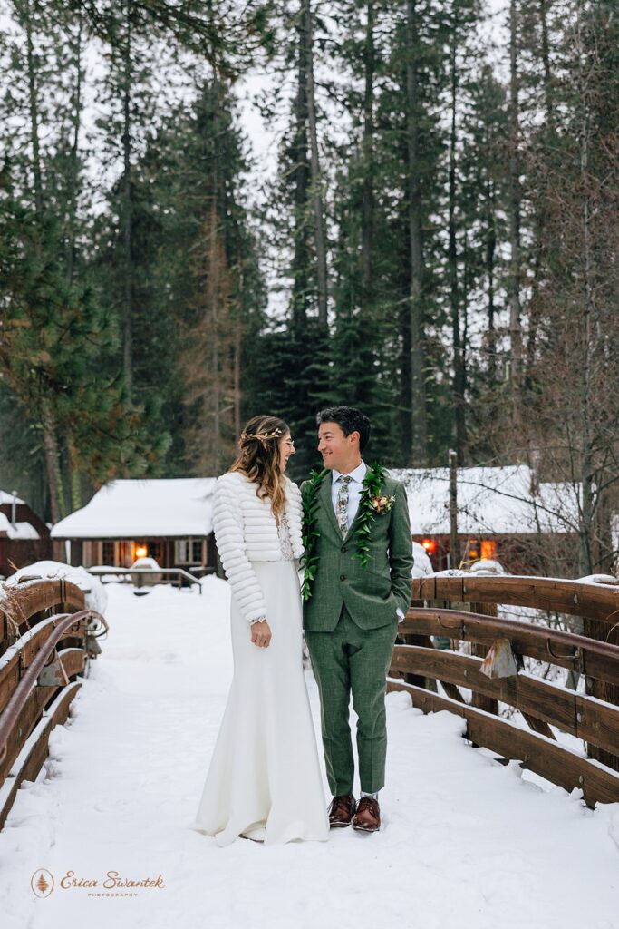 An intimate wedding couple embraces while walking along a snow-covered bridge at Lake Creek Lodge, a wedding location in Bend, Oregon. 