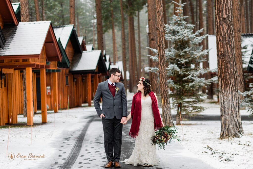 A couple dressed in formal wedding attire walk along a path at FivePine Lodge in Winter. 
