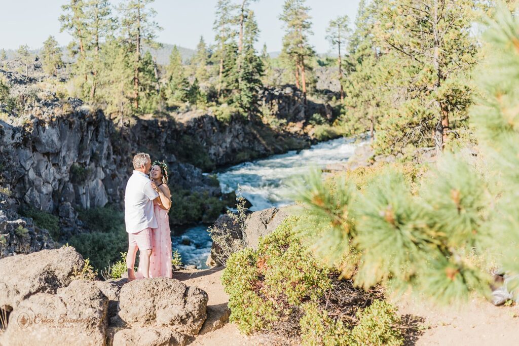An bride and groom stand near Dillon Falls on a cliff's edge during their Oregon elopement. 