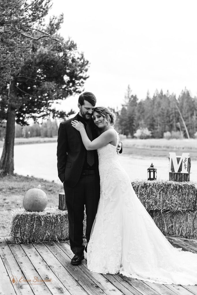 A Sunriver elopement couple embraces on a wooden platform near Fall wedding decorations. 