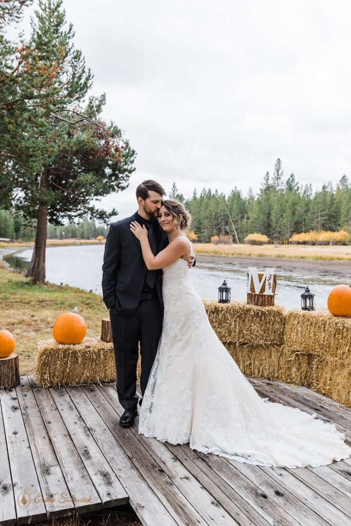 A Fall elopement couple embraces on a wooden platform near autumn wedding decorations along Sunriver in Bend. 