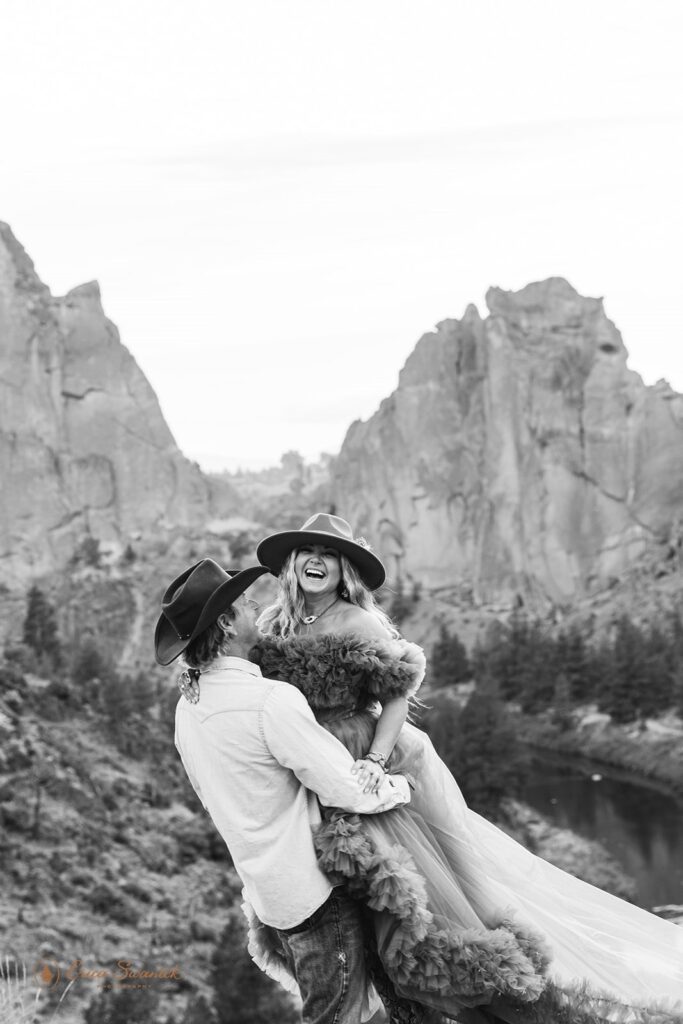 A couple dressed in western wedding attire embraces near a rock formation at Rock Smith State Park. 