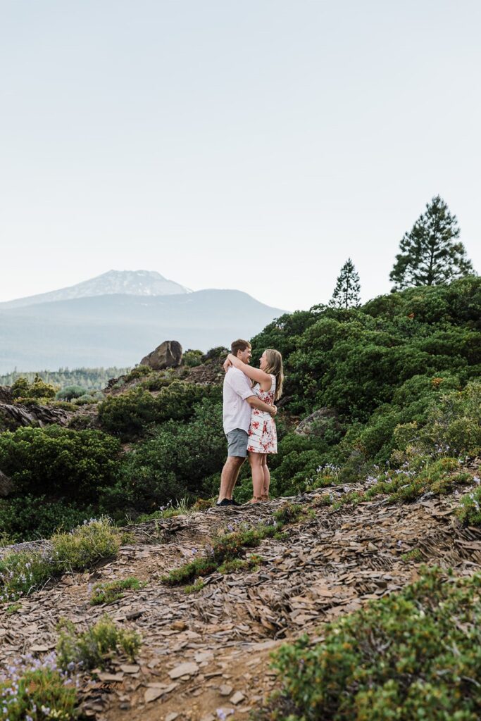 An Oregon elopement couple embraces on an hiking trail with a mountain in the distance at an intimate Bend wedding location.