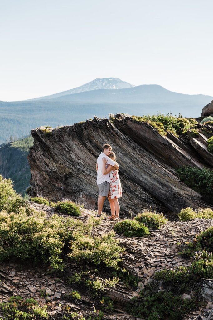 An elopement couple embraces on an Oregon hiking trail with a mountain in the distance at an intimate Bend wedding location.