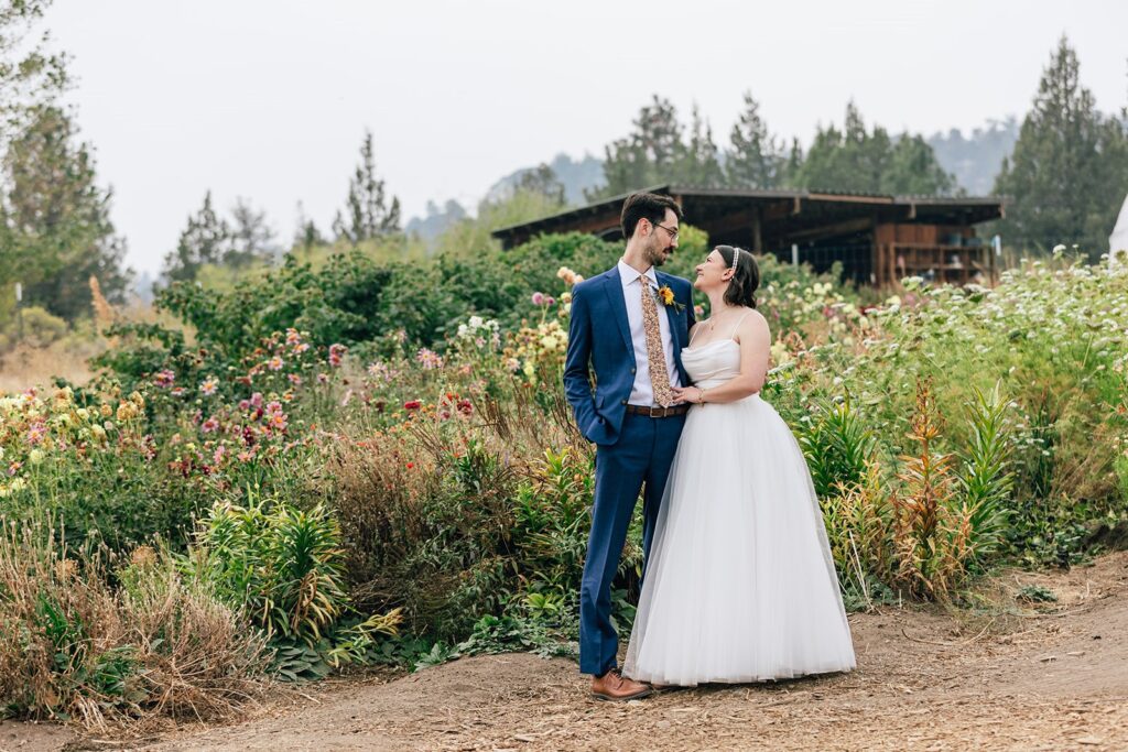 A sustainable wedding couple embraces during wedding portraits near a wildflower garden at Rainshadow Organics. 