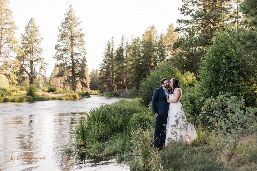 An Oregon elopement couple in formal wedding attire embraces along the banks of the Deschutes River during their intimate outdoor wedding. 