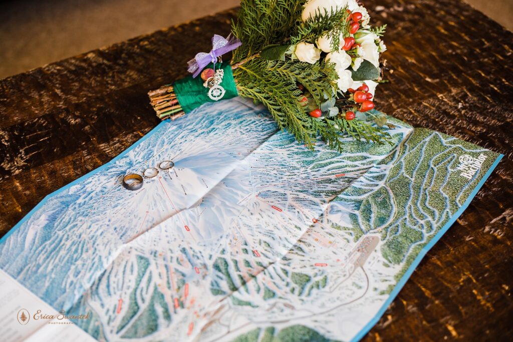 A rose bridal bouquet sits atop a  map of Mt. Bachelor Ski Resort along with wedding bands. 