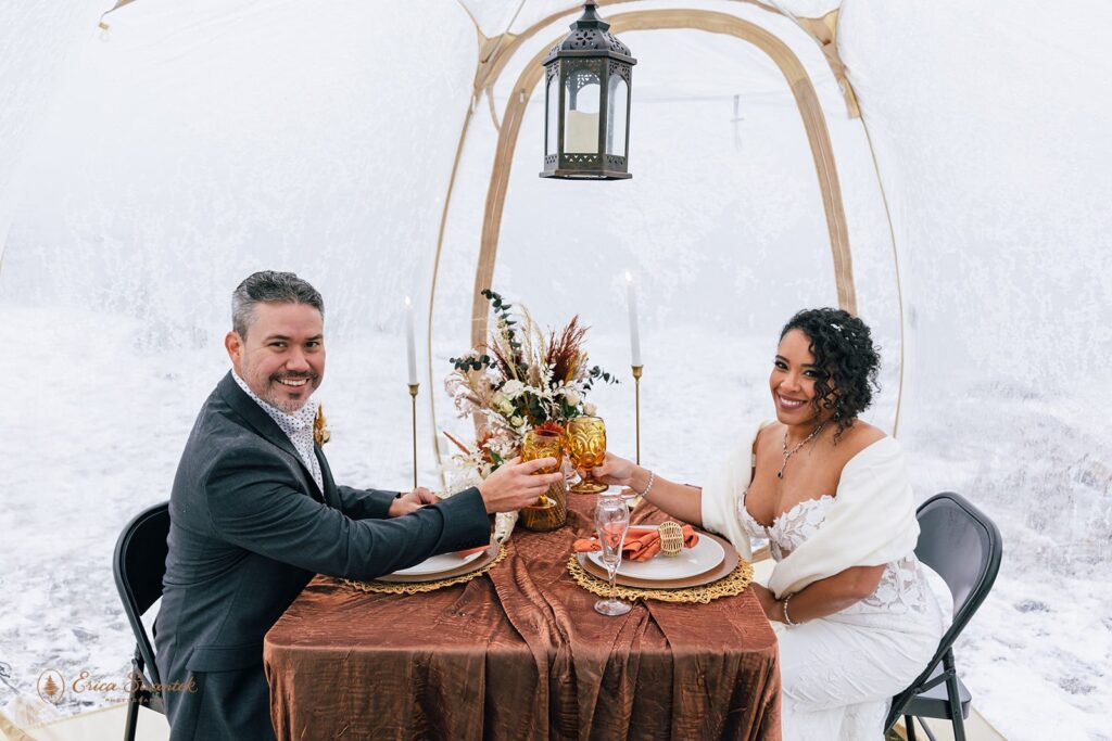 bride and groom enjoying their boho styled picnic under a clear tent set for their winter elopement in columbia river gorge