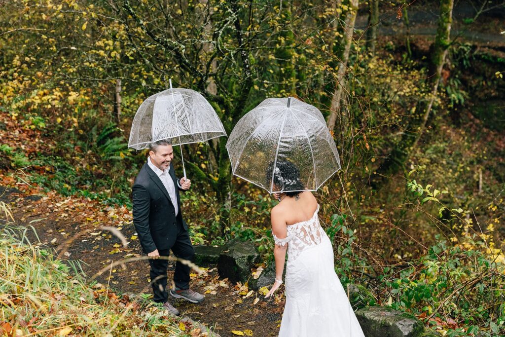 bride and groom elopement first look under clear umbrellas in a forested area