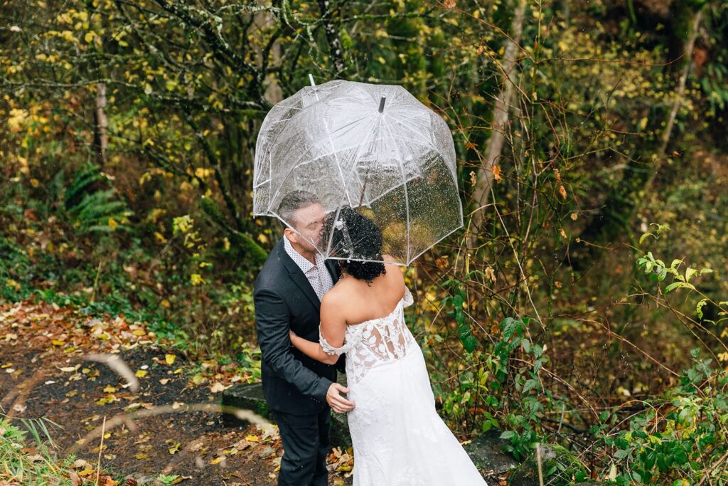 bride and groom elopement first look under clear umbrellas in a forested area