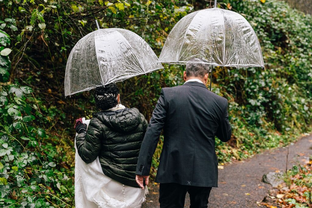 bride and groom under clear umbrellas walking towards a waterfall in columbia river gorge