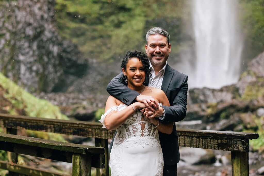 bride and groom posing on a wooden bridge during their Columbia River Gorge elopement with a waterfall in the backdrop