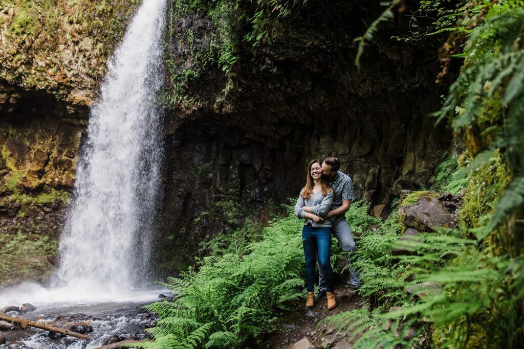 A couple hugging surrounded by mossy cliffs with a waterfall in the backdrop