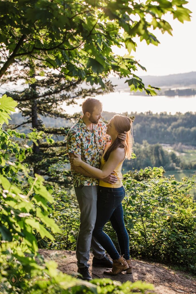 The sun sets behind a couple with the view of the Columbia River behind them from Latourell Falls.