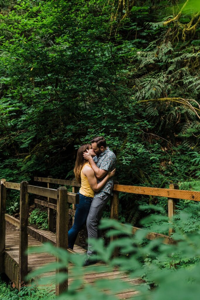 A couple kisses on a bridge at their Latourell Falls hiking adventure engagement session. 