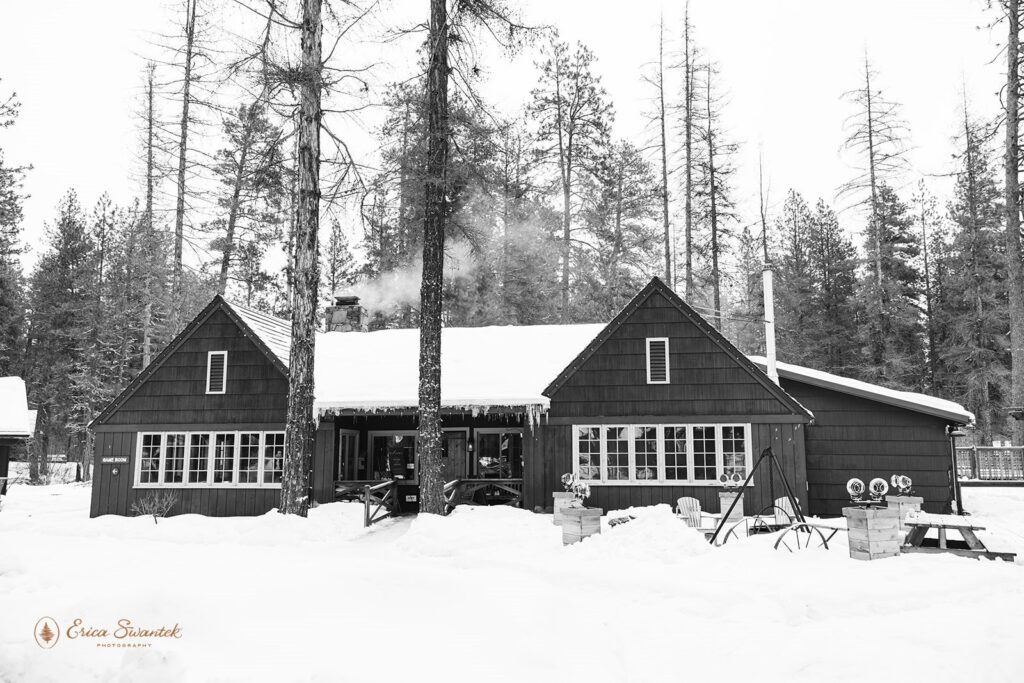 A rustic cabin surrounded by snow, with a beautiful layer of snow covering its roof, black and white photo