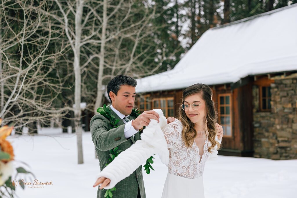 groom helping his bride put on a white fluffy winter jacket