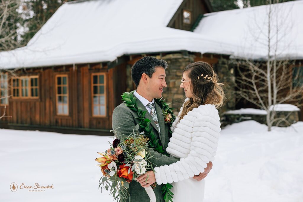 Bride and groom share an intimate moment forehead to forehead in the snow. The bride holds a vibrant bouquet, and the groom wears a green suit with a leaf lei.