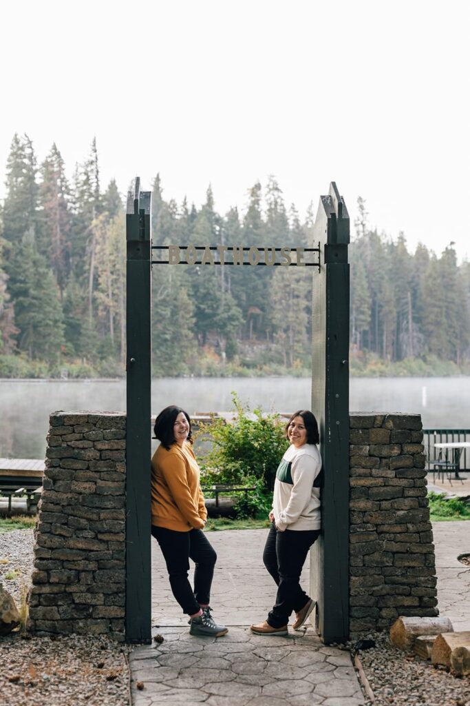 couple stands under the boathouse sign at suttle lake lodge in Oregon.
