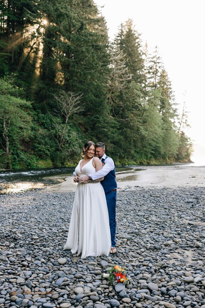 elopement couple standing on a rocky shore with lush forest in the backdrop